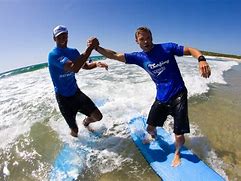 Two men holding hands while riding a surfboard.